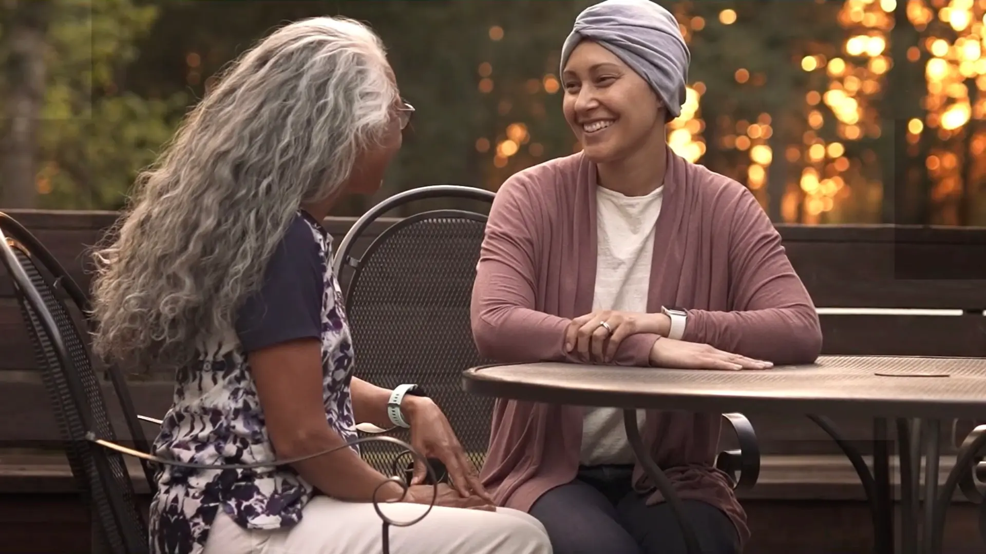 Two women sitting together at an outdoor table, talking and smiling